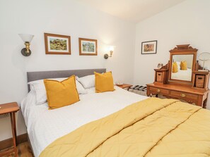 A neatly made bed with a quilted yellow blanket, a wooden nightstand with a lamp, and framed pictures on the wall. - Burlodge (Barnstaple)