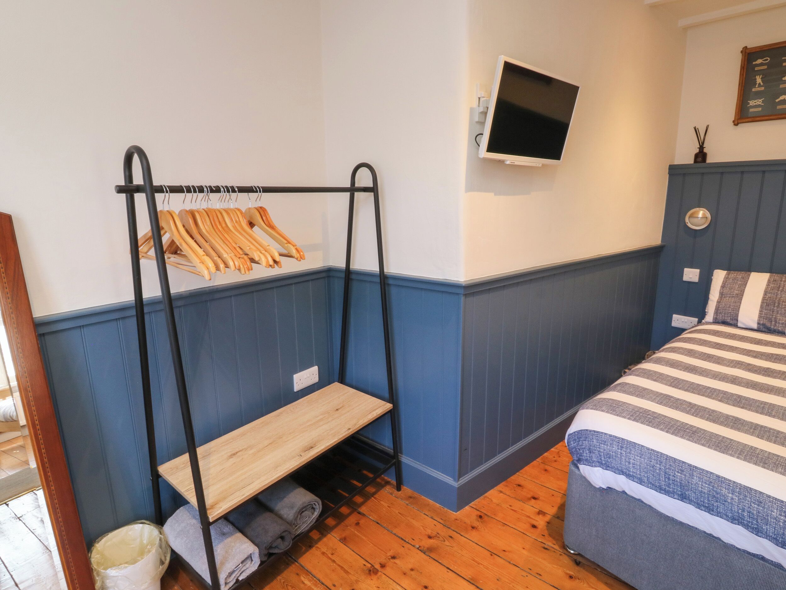 Ein Schlafzimmer mit Etagenbett, einem Holzregal mit Handtüchern, einem flachbildfernseher an der Wand und einem Bett mit gestreifter Bettwäsche.