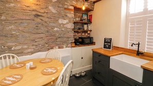 Una cocina acogedora con pared de piedra, vigas de madera en el techo, una mesa redonda de madera con posavasos con forma de pez, un microondas y un letrero que dice 'Bienvenido a The nook'.