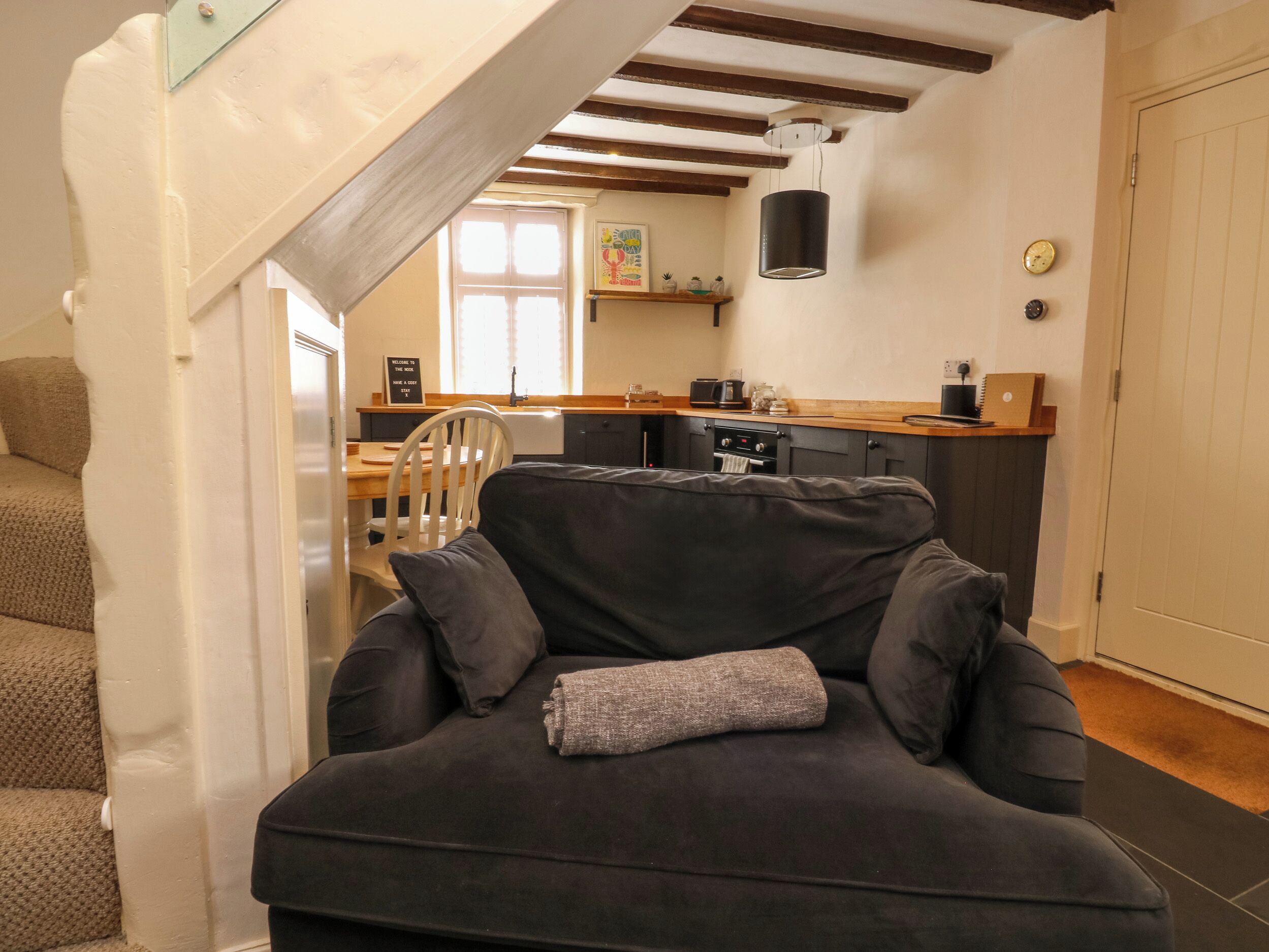 A cozy living area with a dark sofa, a small table, and a kitchen in the background.