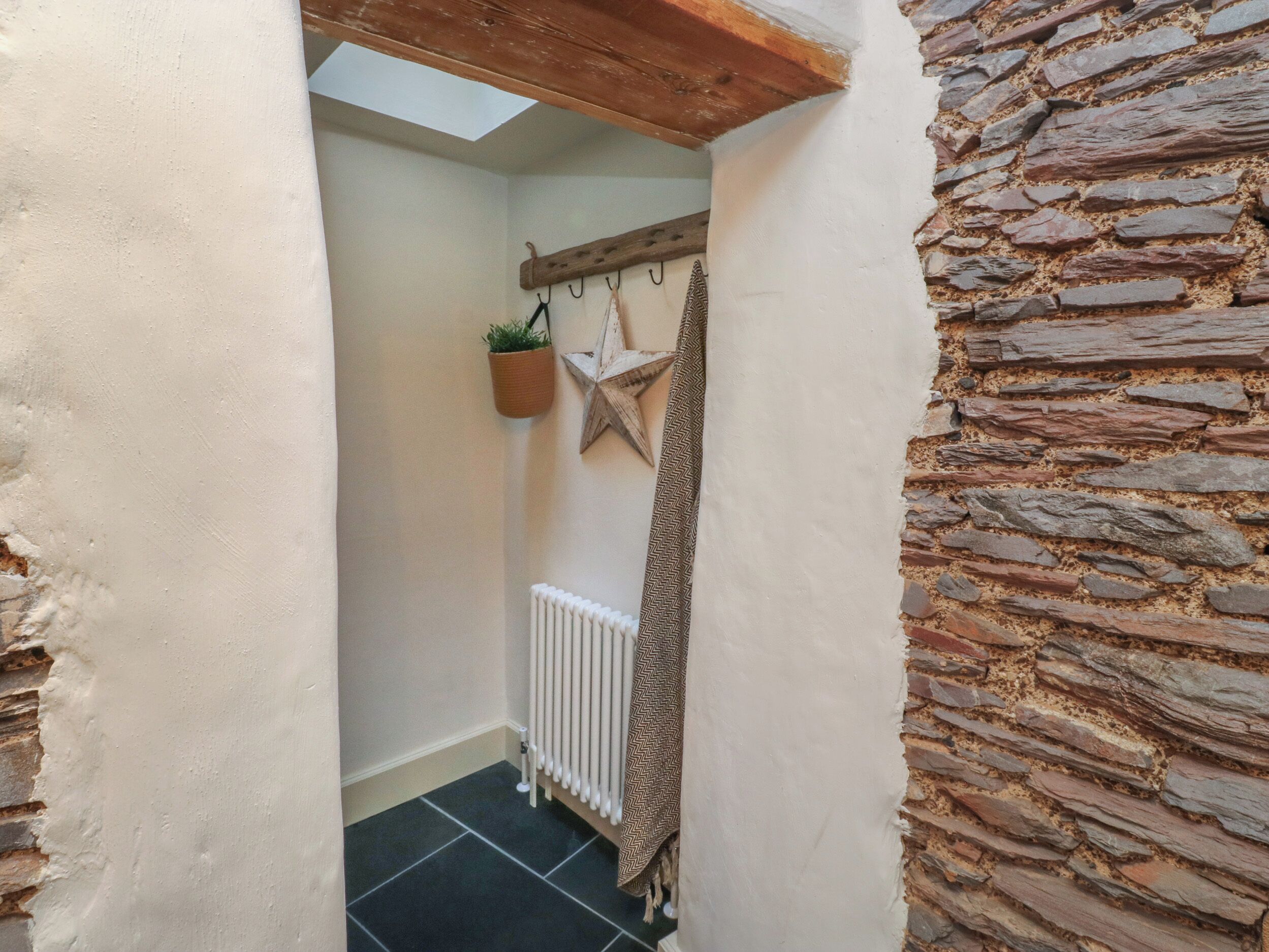 A narrow hallway with a stone wall, a white radiator, a star-shaped decoration, and a hanging plant.
