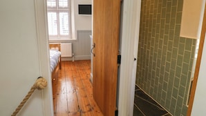 Un pasillo estrecho con suelo de madera que conduce a una habitaci ón con cama y ventana.