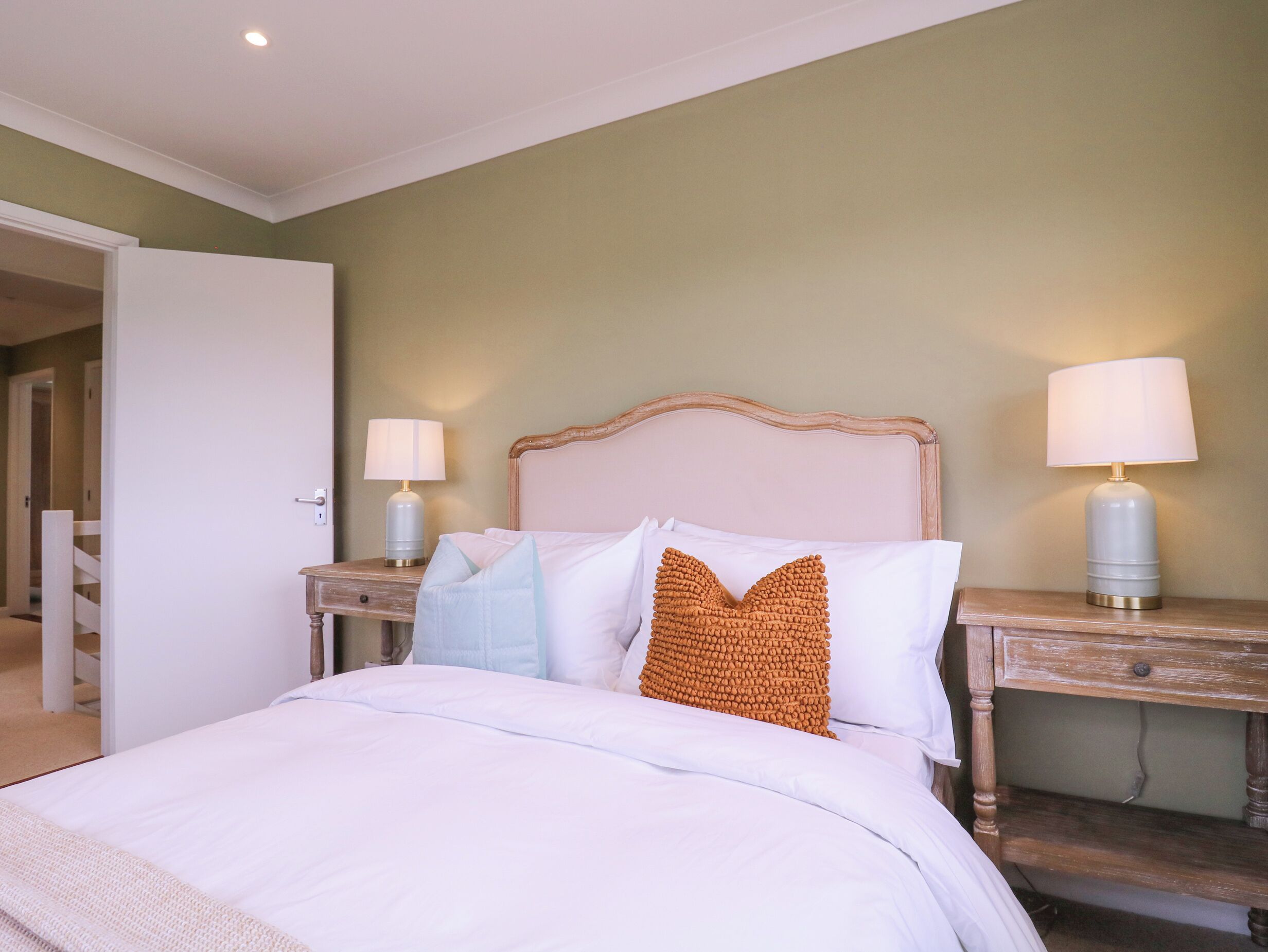 Una habitación de hotel con una cama, dos mesitas de noche con lámparas, un cabecero de madera y una puerta que da a otra habitación.