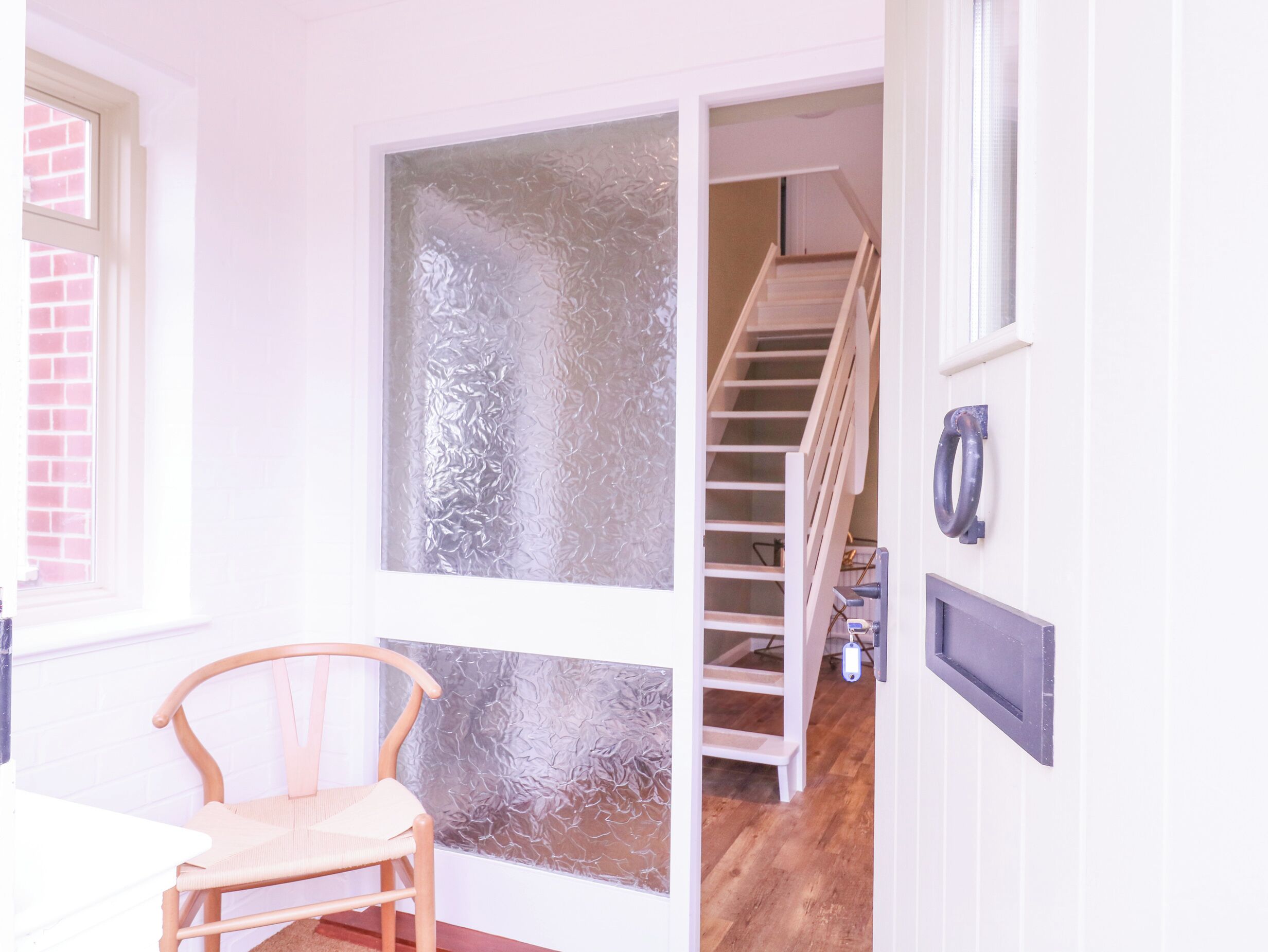 A room with a wooden chair, a frosted glass door, a staircase, and a doorbell.