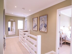 A hallway with a white railing, a mirror, and two framed bird paintings on the wall. - The Farmhouse (Clacton-on-Sea)