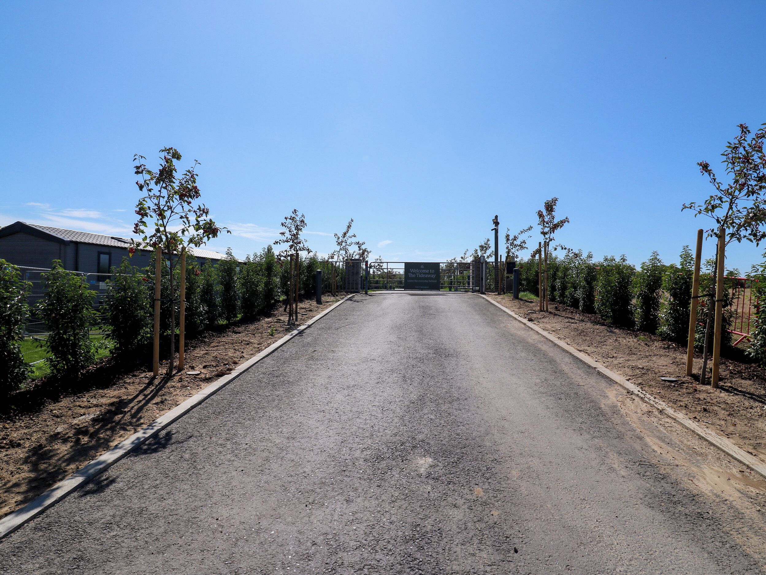 A paved road leading to a gated entrance with a sign welcoming visitors to a property.