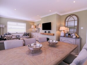 A spacious living area with a large wooden dining table, comfortable seating, a television, and a fireplace. - The Farmhouse (Clacton-on-Sea)