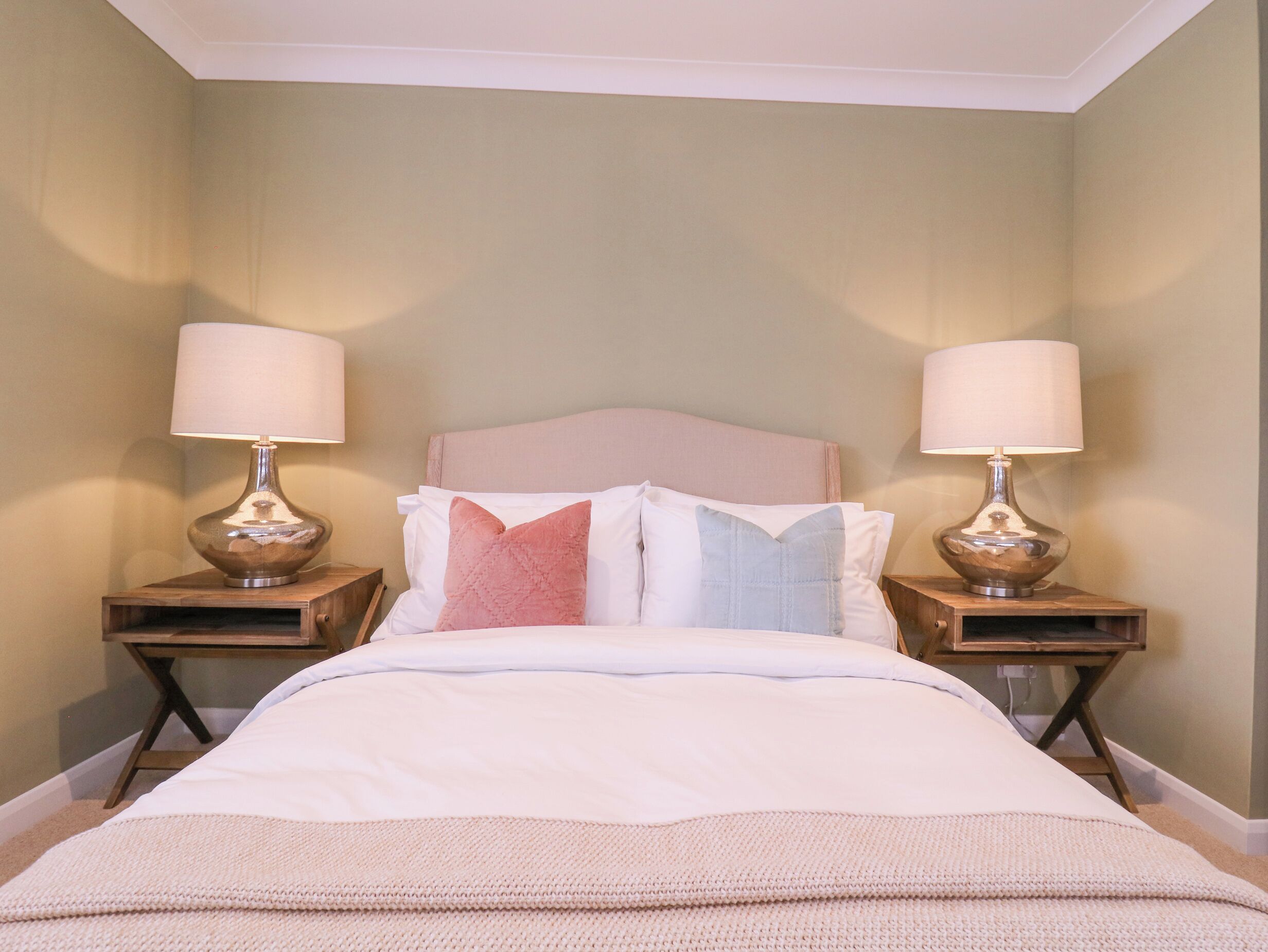 A neatly made bed with a headboard, two bedside tables with lamps, and a plain wall.