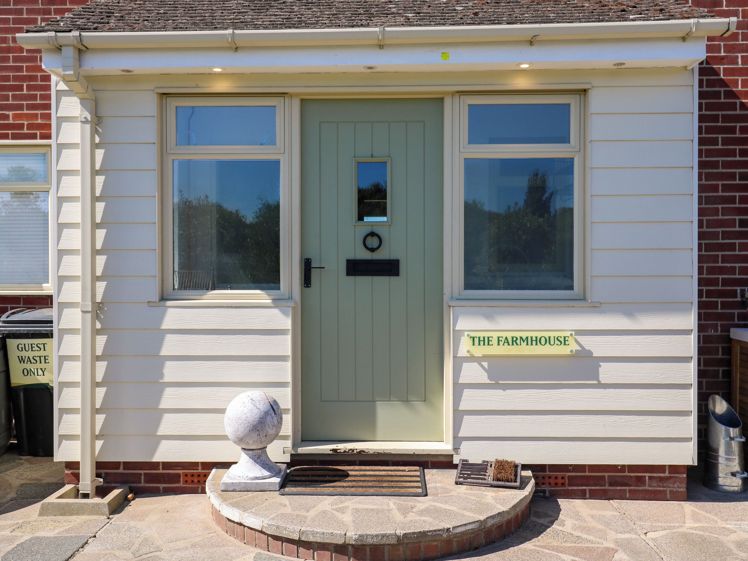 A small, single-story building with a green door, two windows, and a sign reading 'The Farmhouse.'