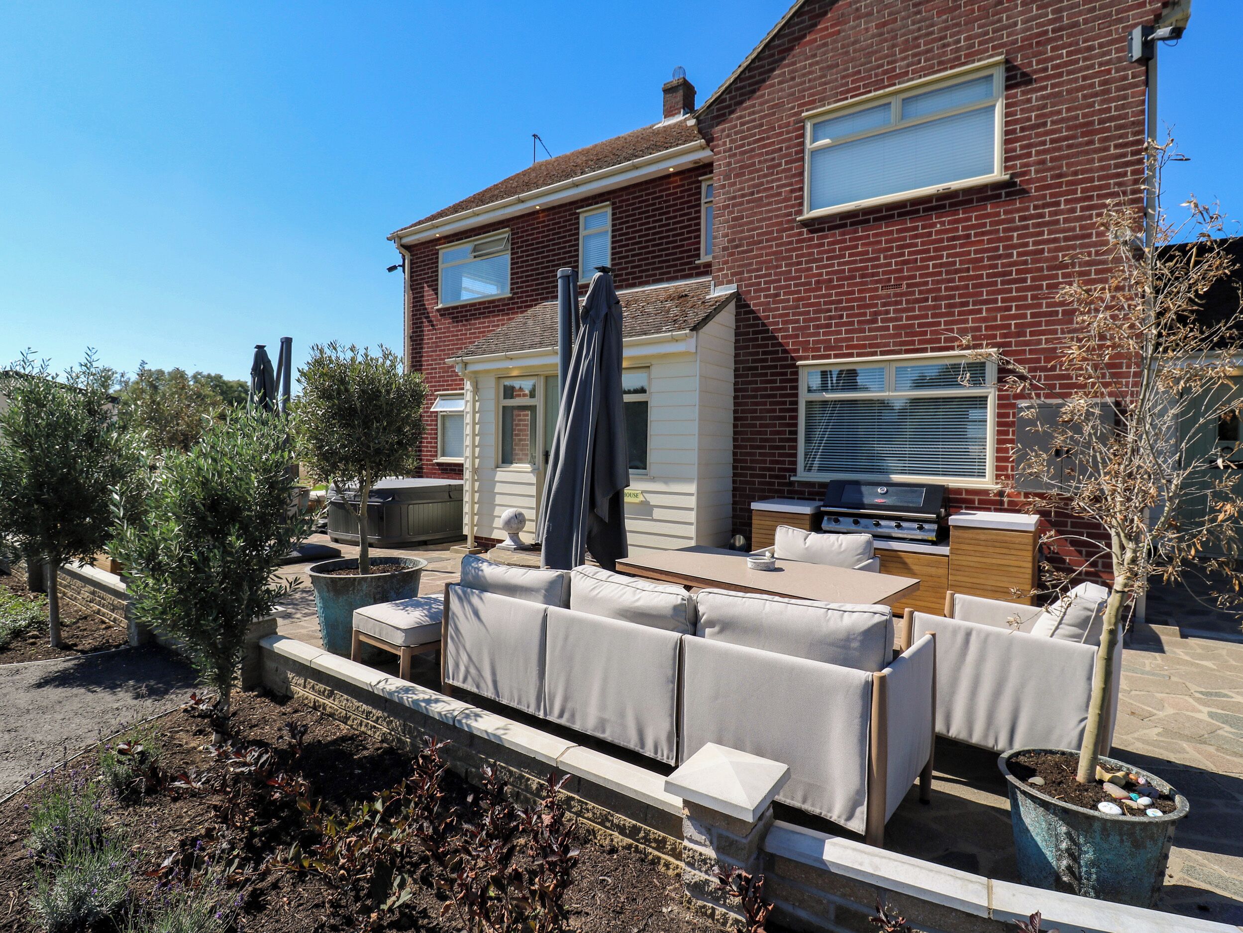 Casa de dos pisos con un patio que cuenta con mobiliario exterior, una parrilla y plantas en macetas.