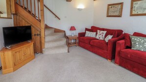 Un salon avec un escalier en bois, un ensemble de canapés rouges, un téléviseur posé sur un meuble en bois et une lampe fixée au mur.