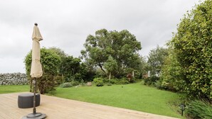 Eine Holzterrasse mit Tisch und Sonnenschirm, umgeben von üppiger Vegetation und Bäumen.