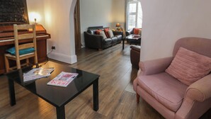 Ein Wohnzimmer mit Klavier, einer Couch, einem Couchtisch und einem rosa Sessel.