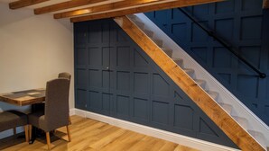 Una habitación con techo de madera, una puerta azul oscuro, una escalera con barandilla de madera y una pequeña mesa con dos sillas.