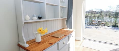Una cocina con armarios blancos, encimera de madera y un florero con flores amarillas. Hay copas de vino en los estantes superiores.