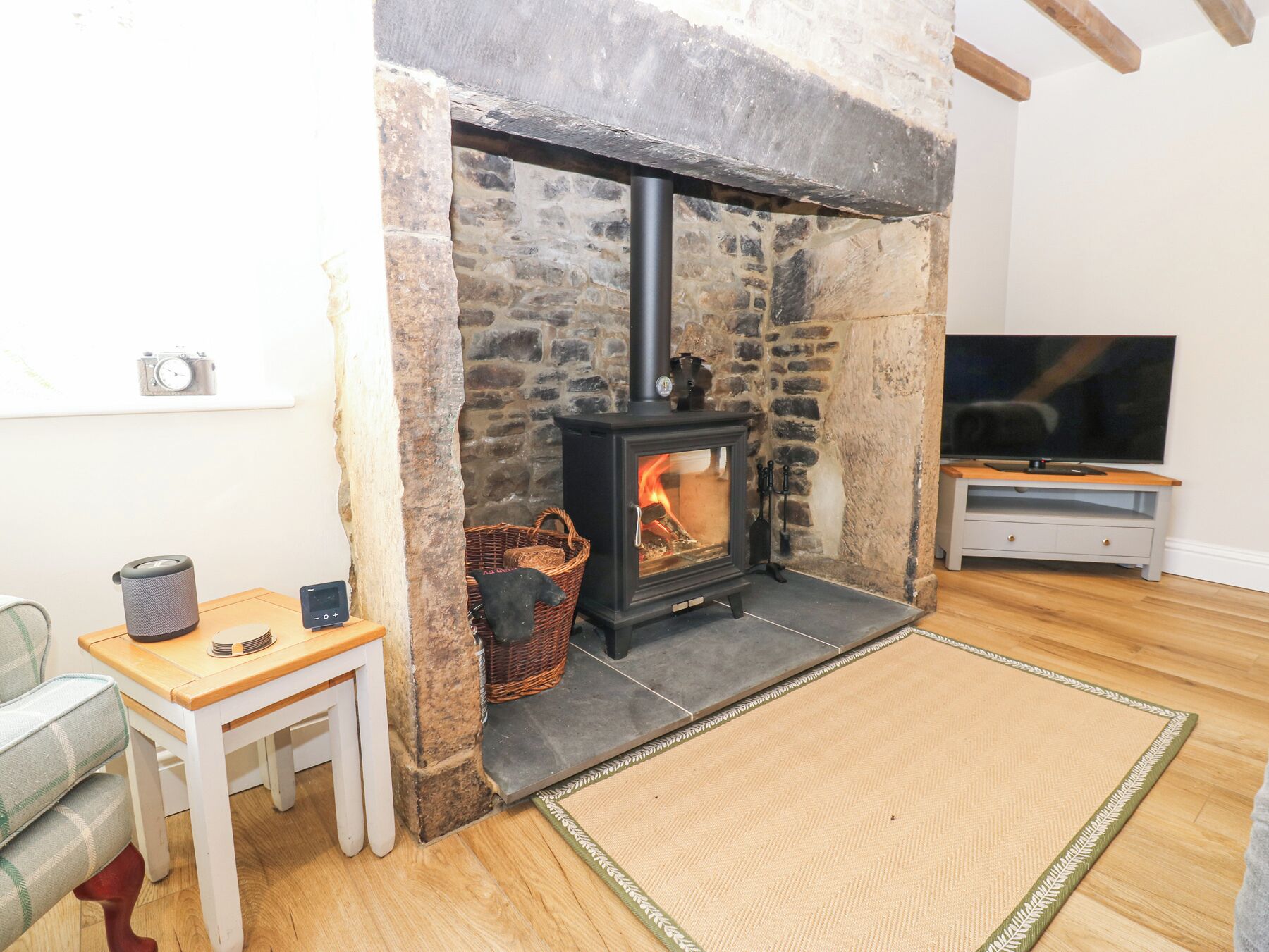 A cozy living room with a stone fireplace, a television, and a small table with a kettle.