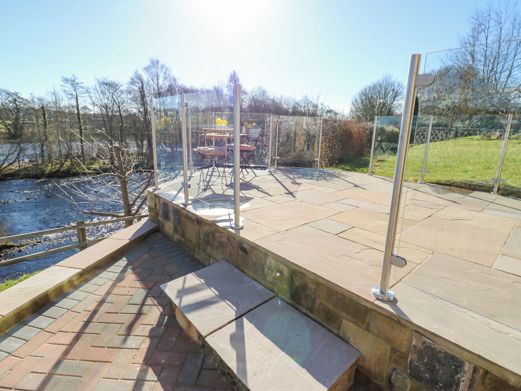 A stone pathway leading to a seating area with a view of a river and trees.