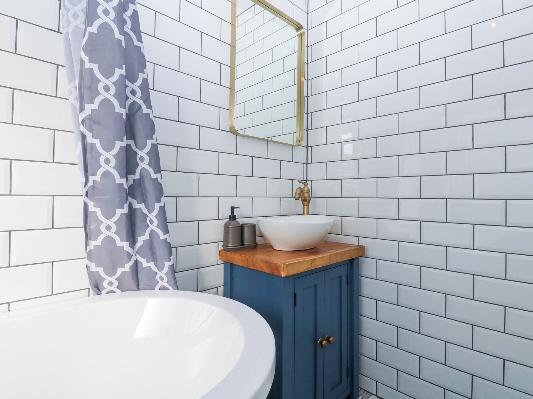 A bathroom with white subway tiles, a white sink, a blue cabinet, and a patterned shower curtain.
