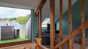A room with a wooden staircase, a view of a green lawn, and a seating area with a table and chairs. - 28 Fore Street (Seaton)