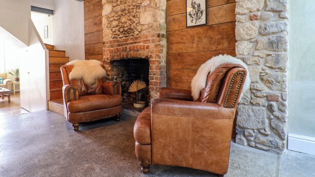 A living room with two leather armchairs, a fireplace, stone walls, and a staircase leading to another room. - 28 Fore Street (Seaton)