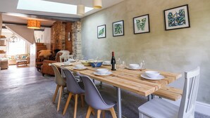 A dining area with a wooden table, chairs, and a stone wall. There are framed artworks on the wall and a chandelier above the table. - 28 Fore Street (Seaton)