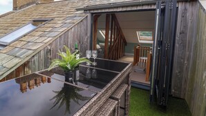 A small, rustic outdoor seating area with a glass-top table, wicker chairs, and a potted fern. - 28 Fore Street (Seaton)