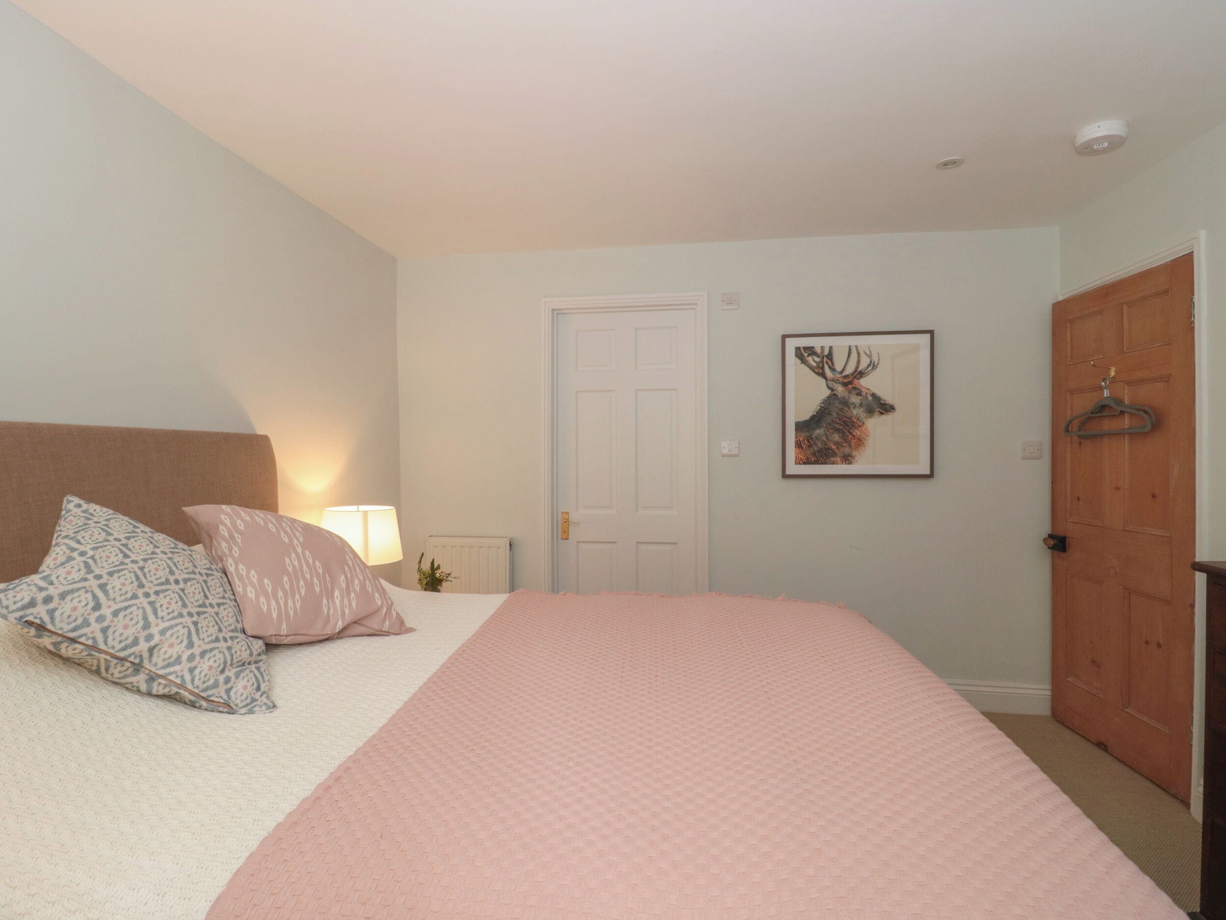 A bedroom with a bed, pillows, a lamp, a door, and a framed picture on the wall.