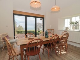 A dining area with a wooden table and chairs, a view of the sea through large windows, and a white radiator on the wall.