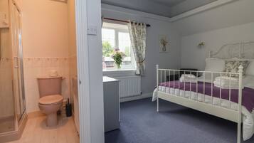 Une chambre à coucher avec un lit blanc, une couvre-lit violette et une fenêtre ornée de rideaux à motifs floraux.