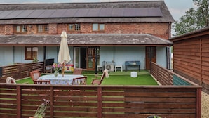 A two-story brick house with a covered patio, solar panels, and a fenced backyard with a table and chairs. - The Barn @ The Elms (Telford)