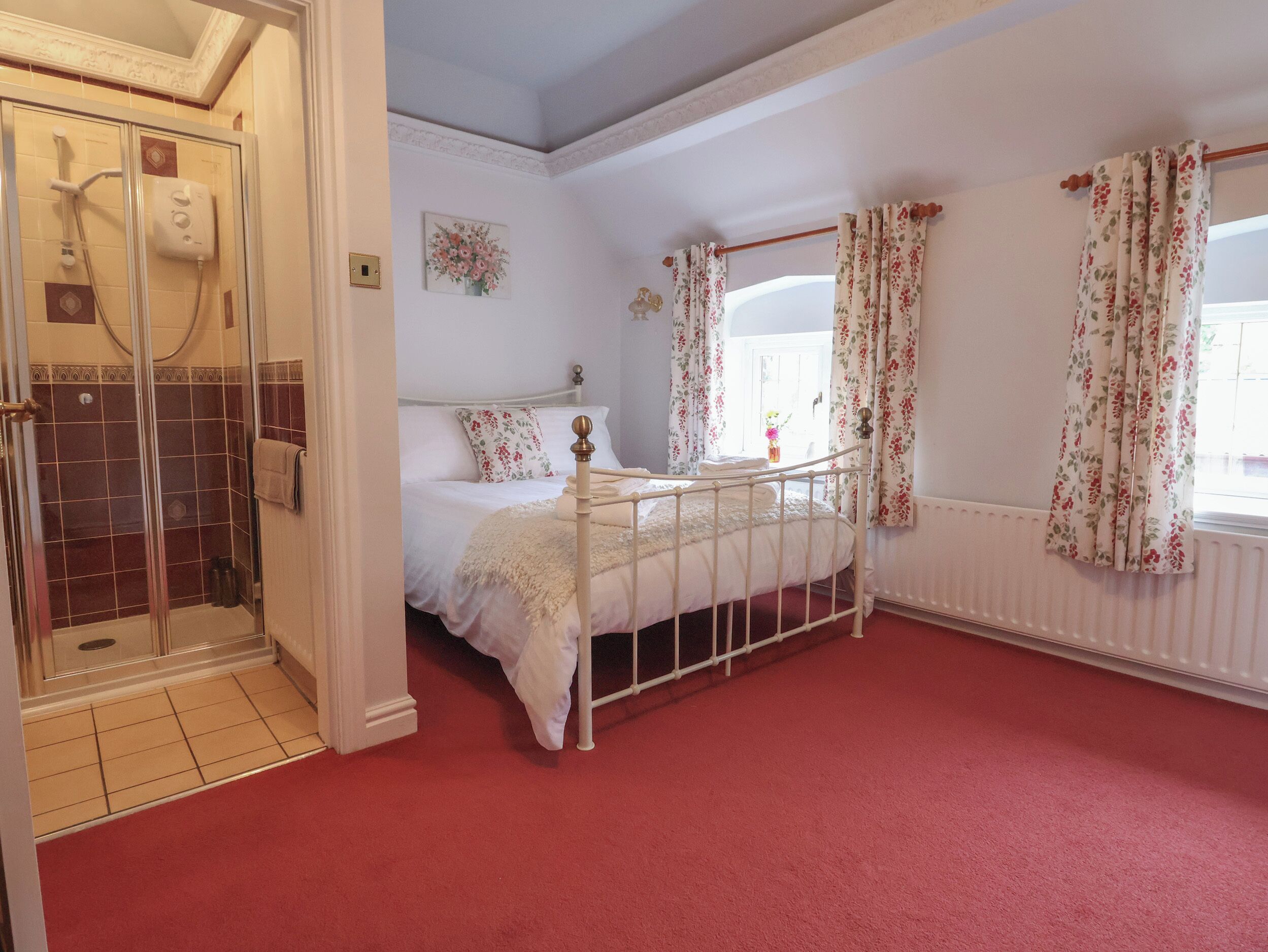 A bedroom with a bed, a shower area, and a window with curtains.