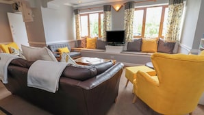 A modern living room with a brown leather sofa, a yellow armchair, and a flat-screen TV. - The Barn @ The Elms (Telford)