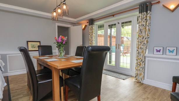 A dining area with a wooden table, black chairs, and a hanging light fixture. - The Barn @ The Elms (Telford)