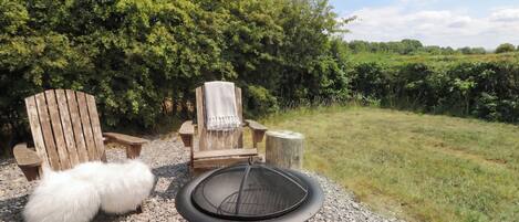 A grill with a mesh screen, two wooden chairs, a white fluffy object, and a gravel path.