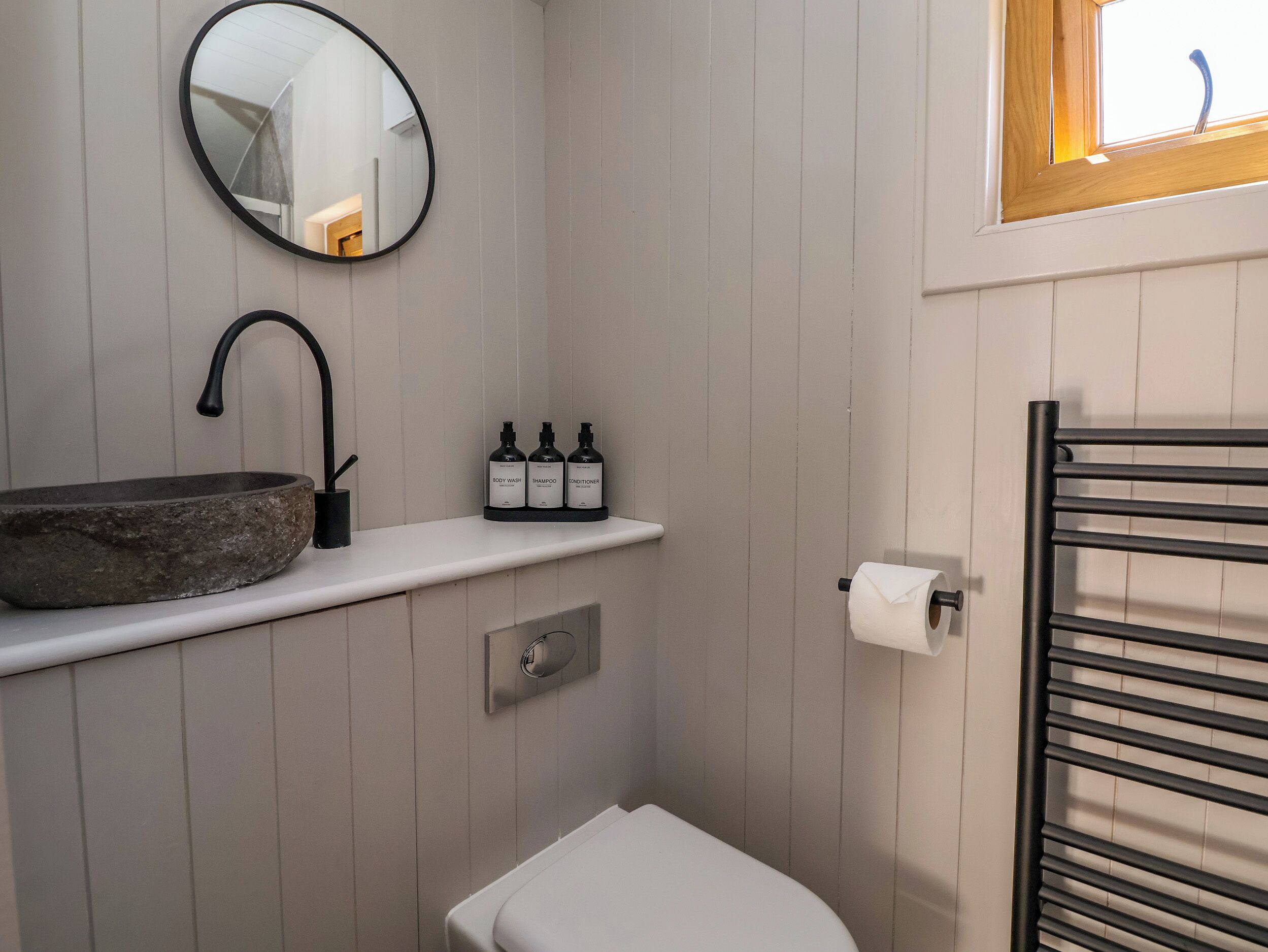 Une salle de bain avec un lavabo en pierre, un miroir, une étagère avec des articles de toilette, des toilettes et un porte-serviettes.