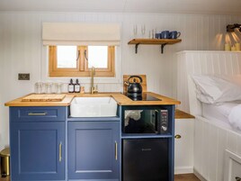 Cocina compacta con lavabo, encimera de madera, armarios azules, hervidor y microondas.