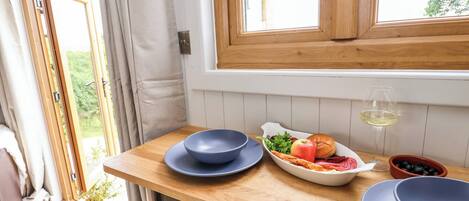 A kitchen with wooden cabinets, a window with curtains, and a table with bowls, a plate, and a glass of wine.
