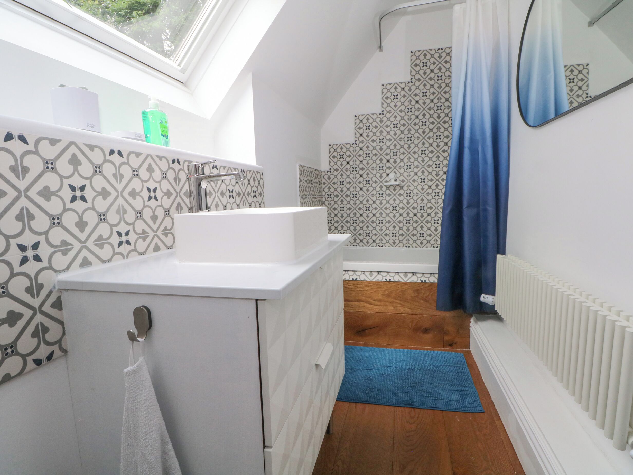 A modern bathroom with a white sink, a towel hanging on a rack, a blue bath mat, and patterned tiles on the walls.