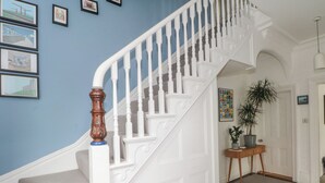 Eine Treppe mit weißen Balustern und einem Holzgeländer, die zu einem Zwischenpodest mit einem Blumentopf und einem gerahmten Bild auf einem kleinen Holztisch führt.