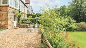 Ein Steinhaus mit Terrasse, weißer Gartenmöbeln und einem gepflegten Garten.