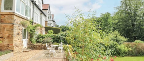 A stone house with a patio, white outdoor furniture, and a well-maintained garden.