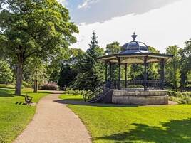 A gazebo with a dome roof and a stone base, surrounded by a well-maintained lawn and trees.