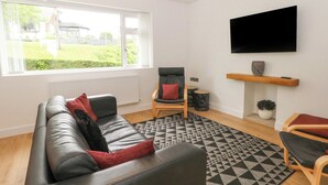 A modern living room with a black leather sofa, a wooden chair, a patterned rug, and a TV mounted on the wall. - Belle Vue (Stoke-on-Trent)