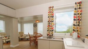 A modern kitchen with a central island, a dining area with chairs, and a view through the window. - Belle Vue (Stoke-on-Trent)