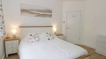 A bedroom with a bed, bedside tables, a nightstand, a door, and a wall-mounted artwork.