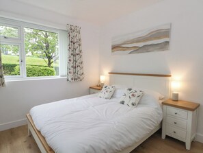 Een slaapkamer met een bed, twee nachtkastjes, gordijnen en een schilderij aan de muur.