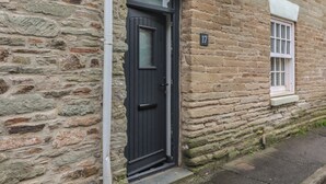 A stone building with a black door and a window with white shutters. - Quarter Deck (Salcombe)