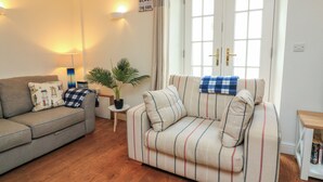 A living room with a sofa, a smaller couch, a lamp, a potted plant, and a bookshelf. - Quarter Deck (Salcombe)