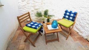 Two wooden chairs with green cushions and blue checkered covers, a small table with a blue vase, a bottle, and two glasses, and a potted plant. - Quarter Deck (Salcombe)