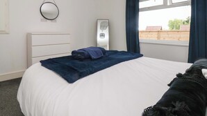 Une chambre à coucher comprenant un lit, une table de chevet, un miroir, une fenêtre avec des rideaux et une vue sur l’extérieur.
